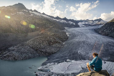 Schweiz, Wallis, Obergoms, Mann auf Felsen sitzend, mit Blick auf Rhonegletscher und Berge - MSUF00322