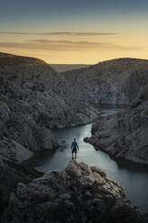 Mann steht auf Felsen und schaut auf den Fluss in einer Schlucht bei Sonnenuntergang - MSUF00353