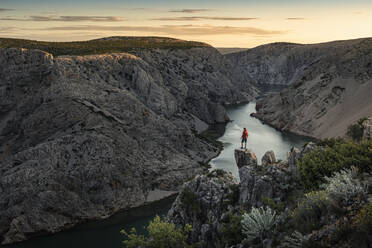 Man standing on rocks and looking at river in canyon at sunset - MSUF00354