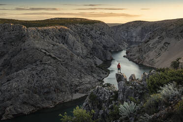 Man standing on rocks and looking at river in canyon at sunset - MSUF00355