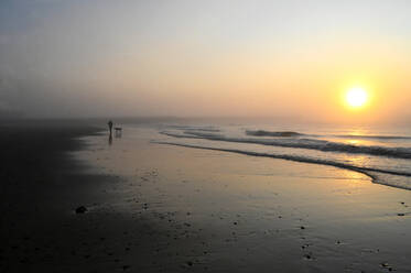 Einsamer Hundespaziergänger bei Sonnenaufgang am Strand bei Ebbe in Walberswick an der Ostküste von England, Suffolk, England, Vereinigtes Königreich, Europa - RHPLF18599