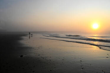 Solitary dog walker at sunrise on the beach at low tide in Walberswick on the east coast of England, Suffolk, England, United Kingdom, Europe - RHPLF18599