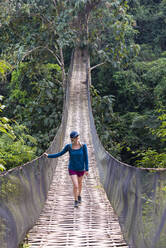 Eine Frau überquert eine prekär aussehende Hängebrücke über den Dschungel in Laos, Indochina, Südostasien, Asien - RHPLF18748