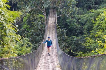 Eine Frau überquert eine prekär aussehende Hängebrücke über den Dschungel in Laos, Indochina, Südostasien, Asien - RHPLF18749