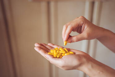 Von oben auf die Handfläche einer anonymen Person, die einen Stapel gelber Vitaminpillen für ein gesundes Lebenskonzept zeigt - ADSF19469