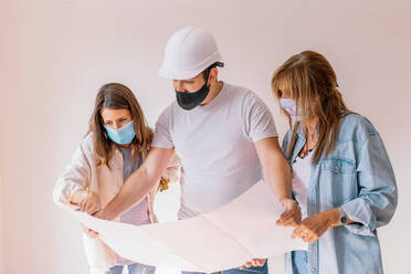 Women in masks and male builder in hardhat examining project of flat renovation - ADSF19493