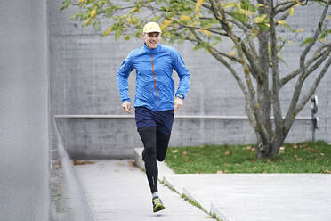 Älterer Mann mit Mütze joggt auf dem Fußweg - JAHF00071