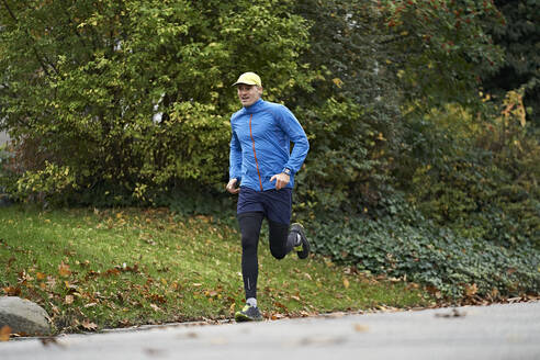 Älterer Mann in Sportkleidung läuft auf einem Fußweg durch Gras - JAHF00073