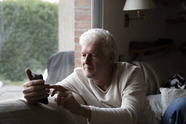 Man using mobile phone while sitting on sofa at home - AFVF07880