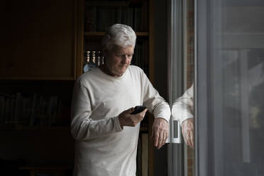 Ältere Mutter telefoniert zu Hause am Fenster stehend - AFVF07881