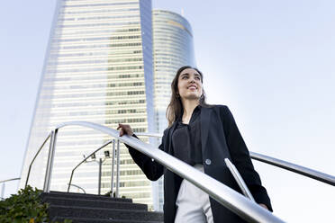 Confident businesswoman holding laptop while standing on staircase i city - JCCMF00274