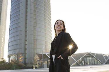 Smiling businesswoman with hand in pocket looking away while standing in city - JCCMF00277