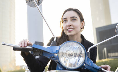 Businesswoman smiling while sitting on scooter - JCCMF00289