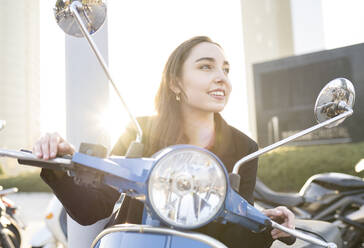 Lächelnde Geschäftsfrau, die auf einem Motorroller sitzend wegschaut - JCCMF00290