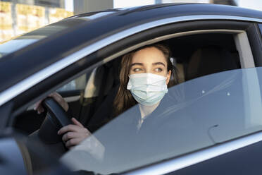 Geschäftsfrau mit Gesichtsschutzmaske, die beim Autofahren während der COVID-19 wegschaut - JCCMF00300