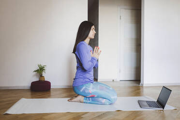 Mid adult woman learning yoga through laptop while sitting at home - EYAF01424