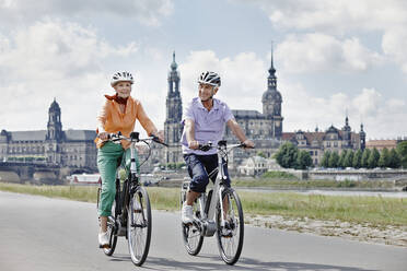 Senior couple cycling electric bicycle on road at Hausmannsturm, Dresden, Germany - RORF02561