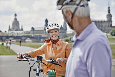 Senior woman with electric bicycle smiling while looking at man while standing at Frauenkirche Cathedral, Dresden, Germany - RORF02568