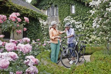 Älterer Mann riecht an einer Rosenblüte, während er neben einer Frau in einem Park in Dresden steht, Deutschland - RORF02575