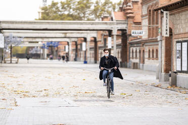 Young man cycling on street with autumn leaves in city during pandemic - GGGF00525