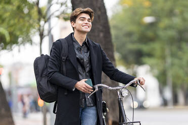 Smiling handsome young man wheeling bicycle in city - GGGF00526