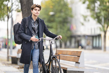 Handsome young man wheeling bicycle in city - GGGF00527