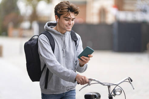 Lächelnder junger Mann, der ein Mobiltelefon benutzt, während er in der Stadt Fahrrad fährt - GGGF00533