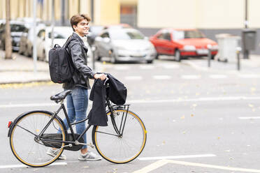 Lächelnder junger Mann mit Fahrrad auf der Straße in der Stadt - GGGF00537