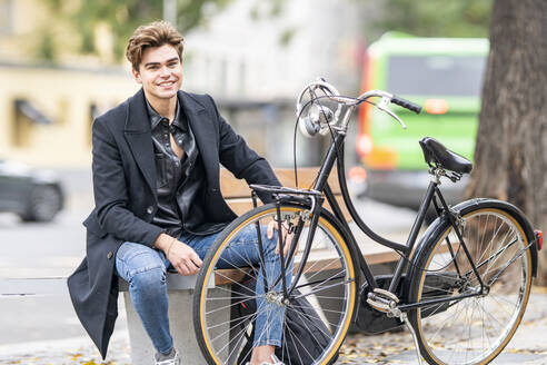 Hübscher junger Mann sitzt auf einer Bank mit dem Fahrrad in der Stadt - GGGF00539