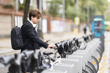 Junger Mann steht in einer Parkstation für Elektrofahrräder in der Stadt - GGGF00542