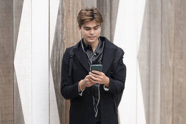 Handsome young man using smart phone against wall - GGGF00565