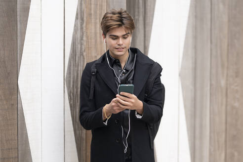 Gut aussehender junger Mann, der sein Smartphone an der Wand benutzt - GGGF00565