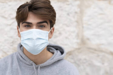 Handsome young man wearing protective face mask against wall during COVID-19 - GGGF00569