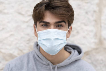 Young man wearing protective face mask against wall during coronavirus - GGGF00570