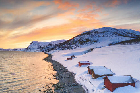 Sonnenuntergang über roten Hütten im Schnee am Porsangerfjord mit Nordkap (Nordkapp) im Hintergrund, Troms og Finnmark, Arktis, Norwegen, Skandinavien, Europa - RHPLF18961