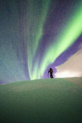 Mann mit Stativ beim Fotografieren des Nordlichts (Aurora Borealis) im Schnee stehend, Skarsvag, Nordkapp, Troms og Finnmark, Norwegen, Skandinavien, Europa - RHPLF18989