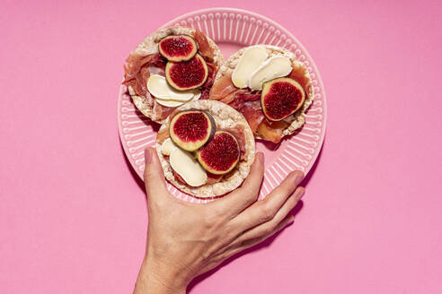 Hand of woman picking up rice cake with serrano ham, cheese and fig slices - GEMF04483