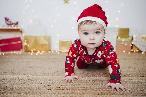Niedliches kleines Mädchen mit Weihnachtsmannmütze krabbelt auf dem Boden zu Hause während Weihnachten - EBBF01940