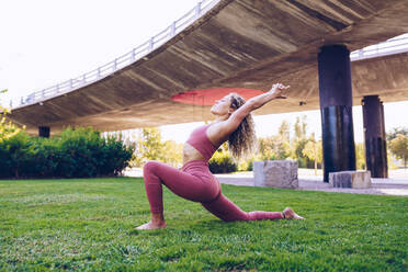 Ganzkörper-Seitenansicht von schlanken flexiblen weiblichen in activewear üben Yoga-Pose auf grünem Rasen im Park - ADSF19564