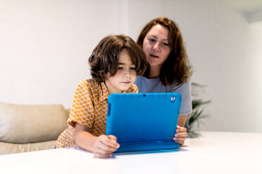 Kind mit hellem Netbook am Tisch neben der zufriedenen Mutter im Haus - ADSF19583