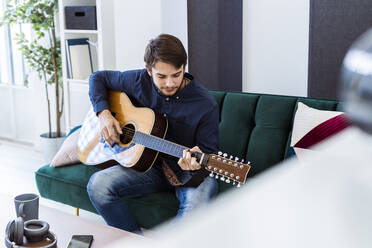 Musiker spielt Gitarre, während er auf dem Sofa im Studio sitzt - GIOF10174