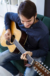 Gitarrist spielt Akustikgitarre, während er auf dem Sofa im Studio sitzt - GIOF10177