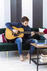 Junger Gitarrist bei der Probe, während er im Studio sitzend Gitarre spielt - GIOF10179