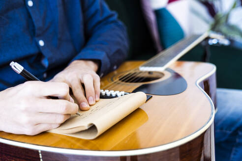Songschreiber schreibt Musik auf einem Notizblock, während er mit einer Gitarre im Studio sitzt - GIOF10184