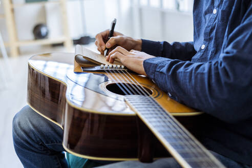 Male composer writing in note pad while sitting at studio - GIOF10186