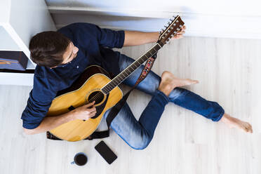 Musiker spielt Akustikgitarre, während er in einem Studio auf dem Boden sitzt - GIOF10189