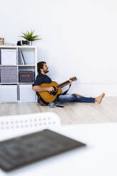 Musician playing guitar while sitting on floor at studio - GIOF10191