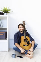 Lächelnder Musiker mit Gitarre auf dem Boden im Studio sitzend - GIOF10193