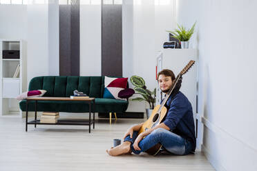 Musiker lächelt, während er mit seiner Gitarre auf dem Boden im Studio sitzt - GIOF10194