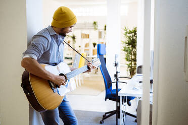 Musician playing guitar while standing at studio - GIOF10203